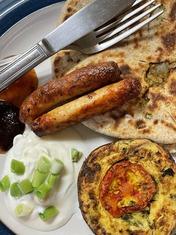 蓝边盘子里有自制的gobi aloo paratha，美味的面包里塞满了garam masala土豆，花椰菜和洋葱配香肠，迷你蛋挞，酸奶和切碎的葱，视野开阔